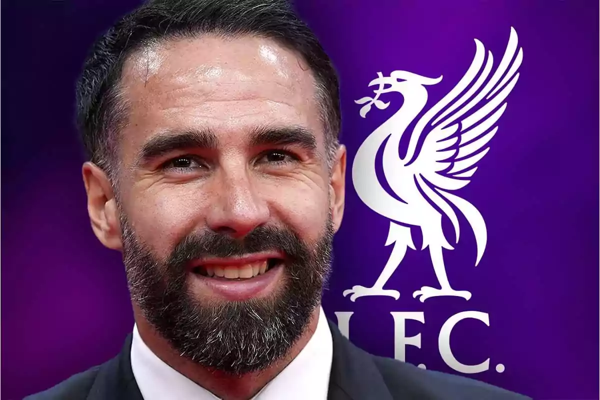 Bearded man in a suit smiles in front of a purple background with the Liverpool FC logo.