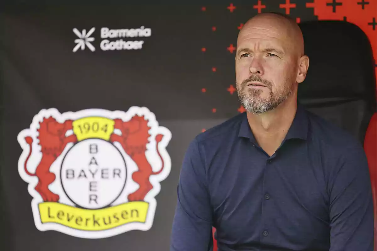 Hombre calvo con barba sentado frente al escudo del Bayer Leverkusen en un estadio Hombre calvo con barba sentado frente al escudo del Bayer Leverkusen en un estadio