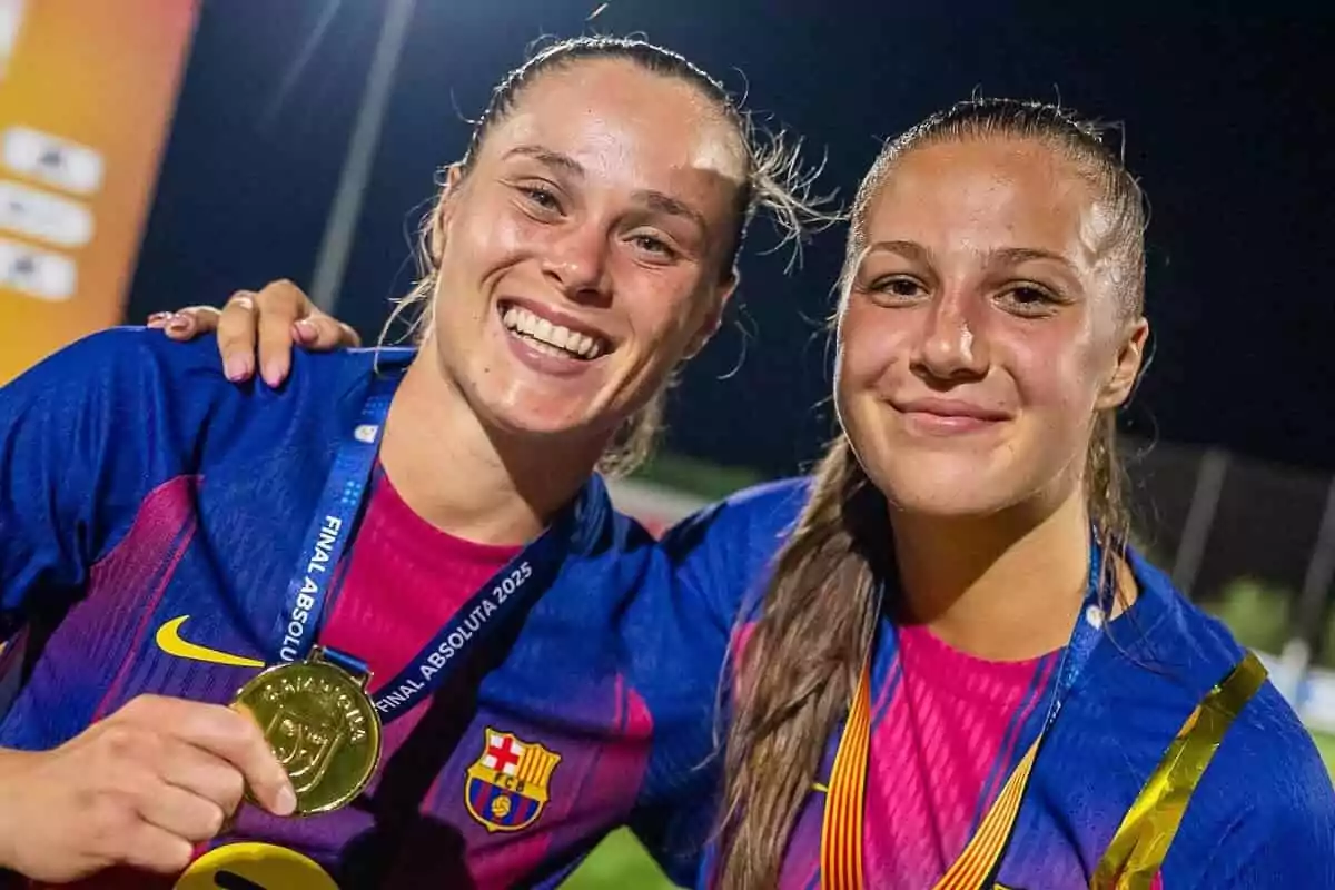 Two FC Barcelona women's players smile and pose together after winning a medal in a soccer final. Two FC Barcelona women's players smile and pose together after winning a medal in a soccer final.