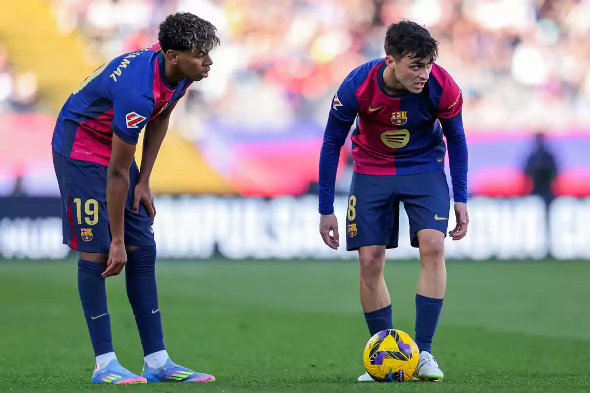 Two Barcelona players in blue and red uniforms get ready to execute a play on the field during a match. Two Barcelona players in blue and red uniforms get ready to execute a play on the field during a match.