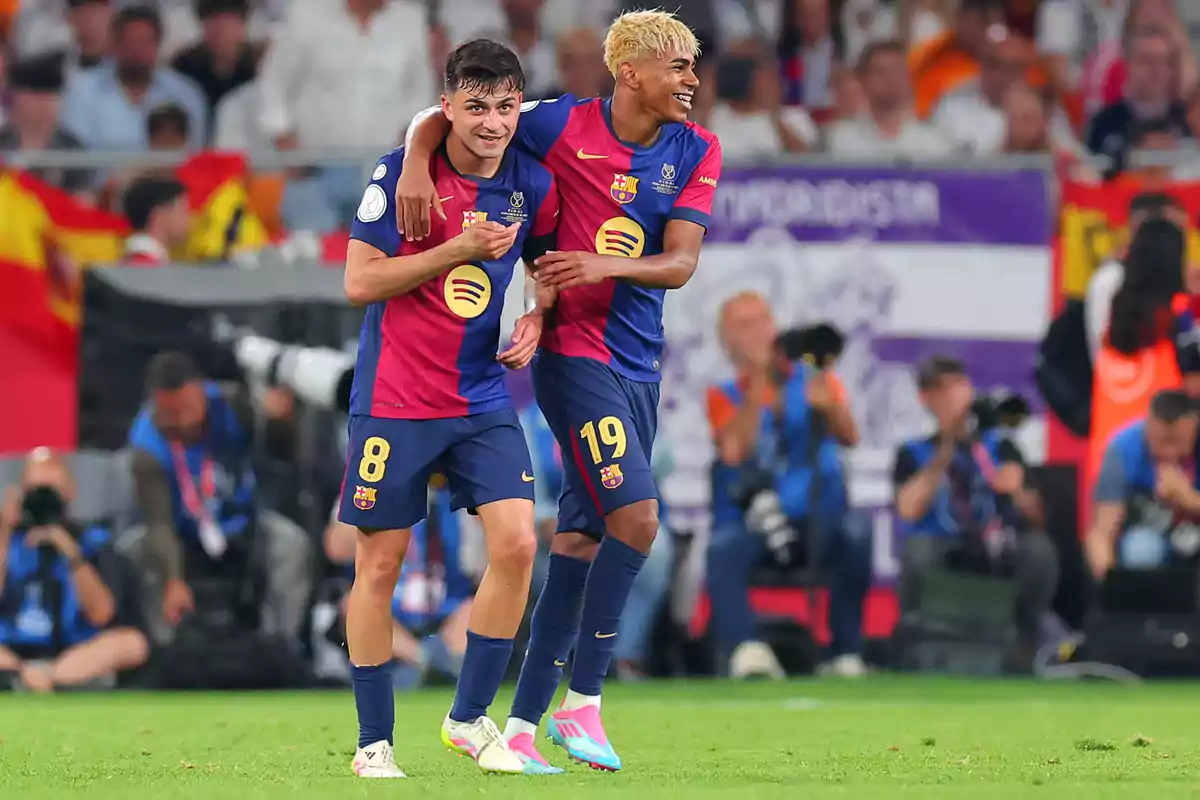 Two Barcelona players celebrate together on the field during a match while smiling and hugging. Two Barcelona players celebrate together on the field during a match while smiling and hugging.