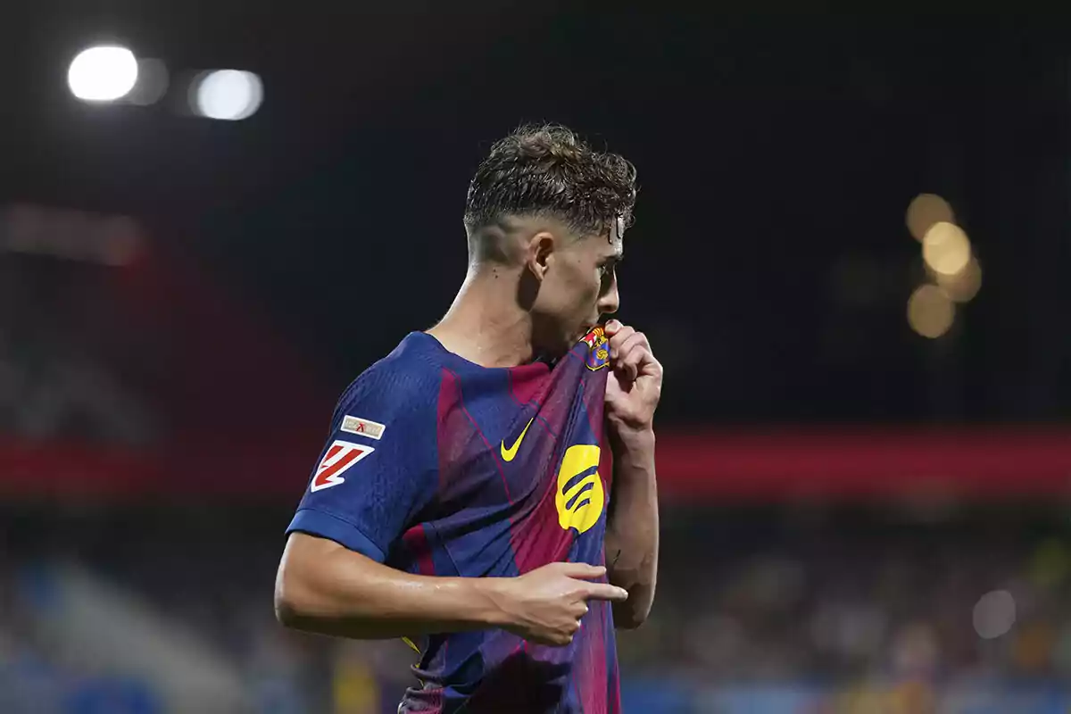 Jugador de fútbol besando el escudo de su camiseta del FC Barcelona durante un partido nocturno Jugador de fútbol besando el escudo de su camiseta del FC Barcelona durante un partido nocturno