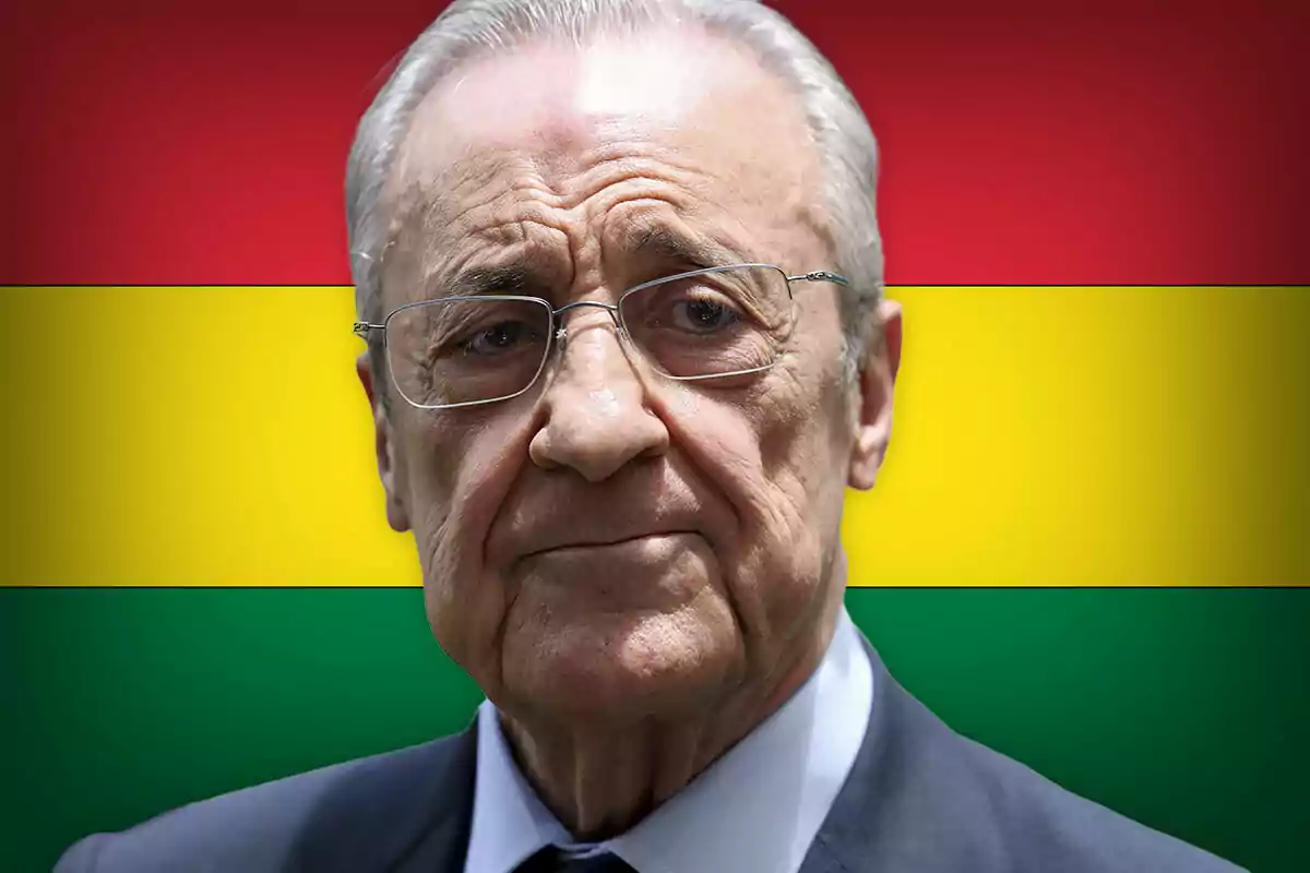 Older man with glasses and a suit in front of a background flag with red, yellow, and green stripes