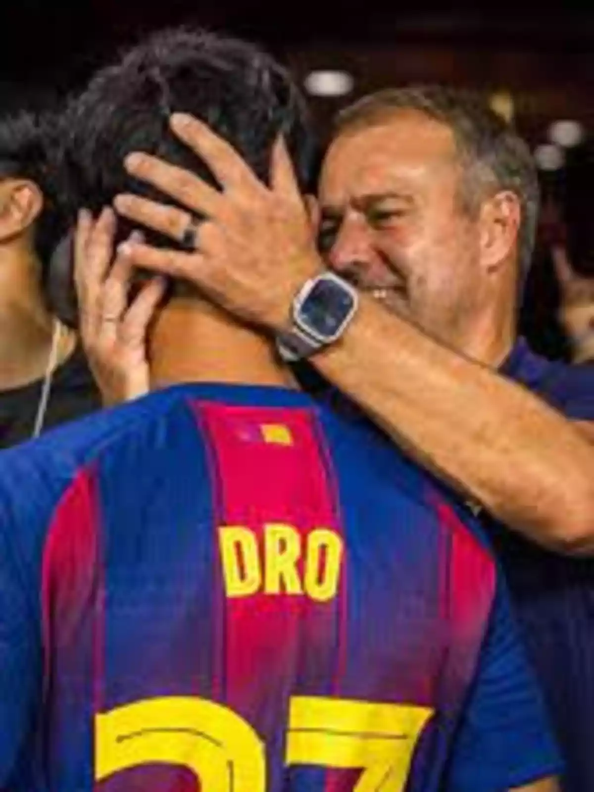 Smiling man hugs the head of a player wearing a blue and red jersey with the name DRO and the number 27 with both hands. Smiling man hugs the head of a player wearing a blue and red jersey with the name DRO and the number 27 with both hands.