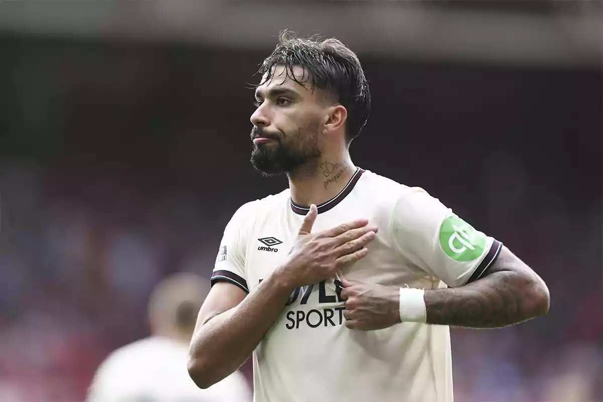 Soccer player with a beard and tattoos on his neck and arm celebrating with his hand on his chest during a match, wearing a white uniform Soccer player with a beard and tattoos on his neck and arm celebrating with his hand on his chest during a match, wearing a white uniform