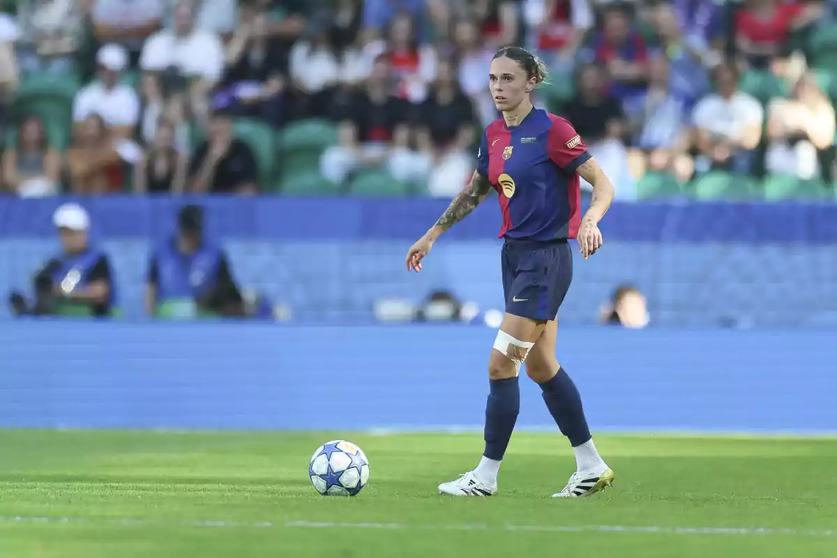 Barcelona women's footballer on the field during a match with the ball nearby and spectators in the stands in the background Barcelona women's footballer on the field during a match with the ball nearby and spectators in the stands in the background