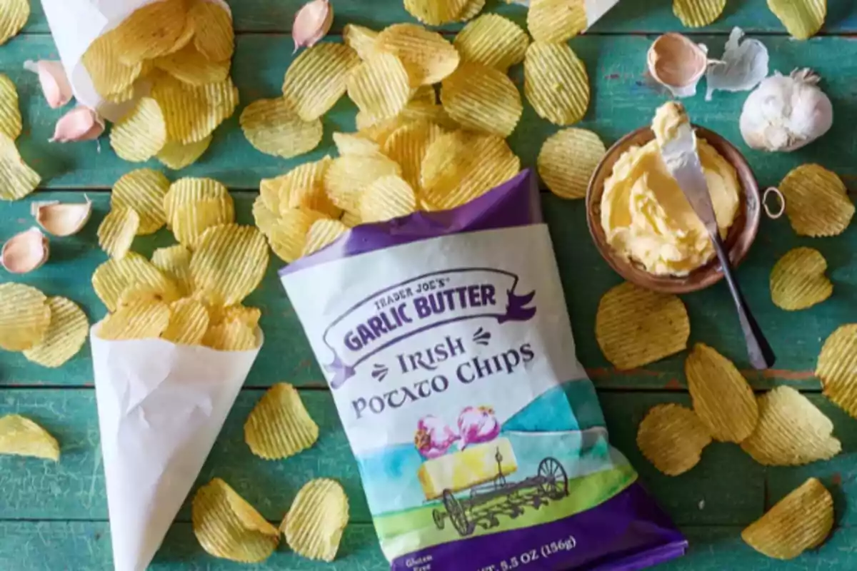 Bag of butter and garlic flavored potato chips on a green table surrounded by potatoes, garlic cloves, and a container of butter Bag of butter and garlic flavored potato chips on a green table surrounded by potatoes, garlic cloves, and a container of butter