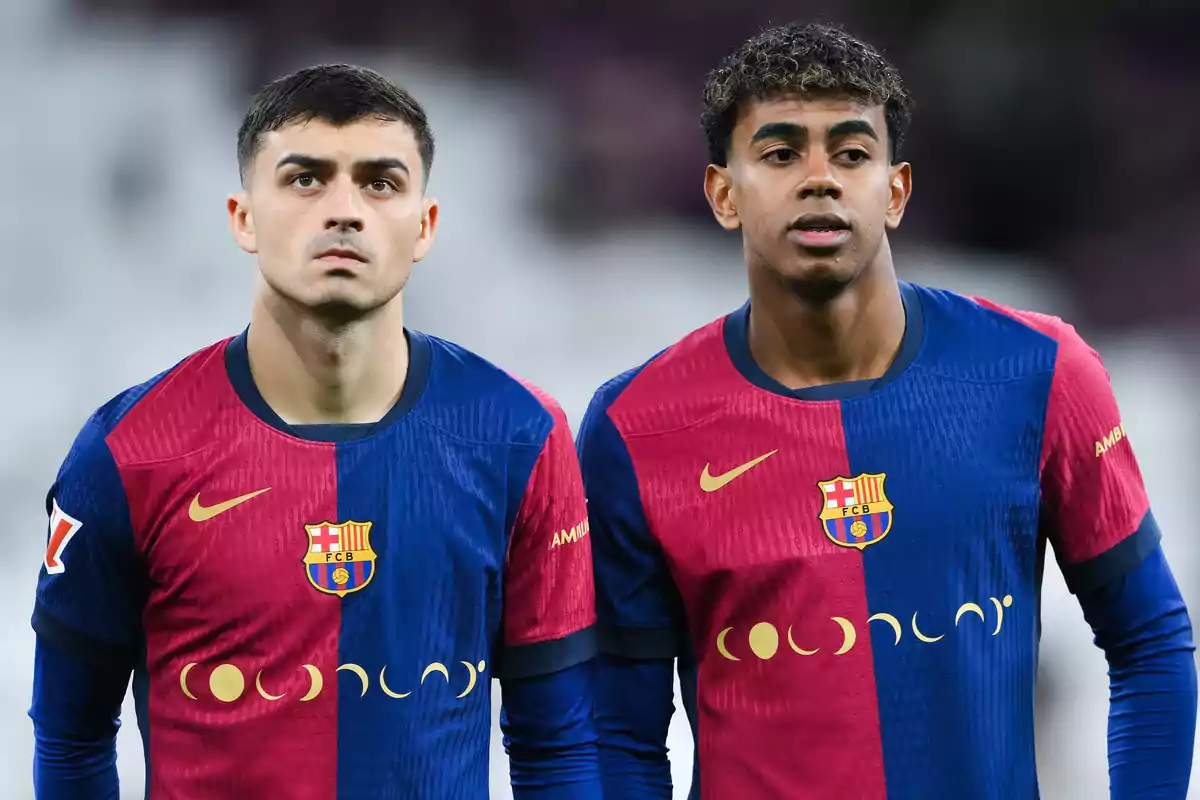 Two FC Barcelona players in blue and red uniforms pose together on the field before a match.