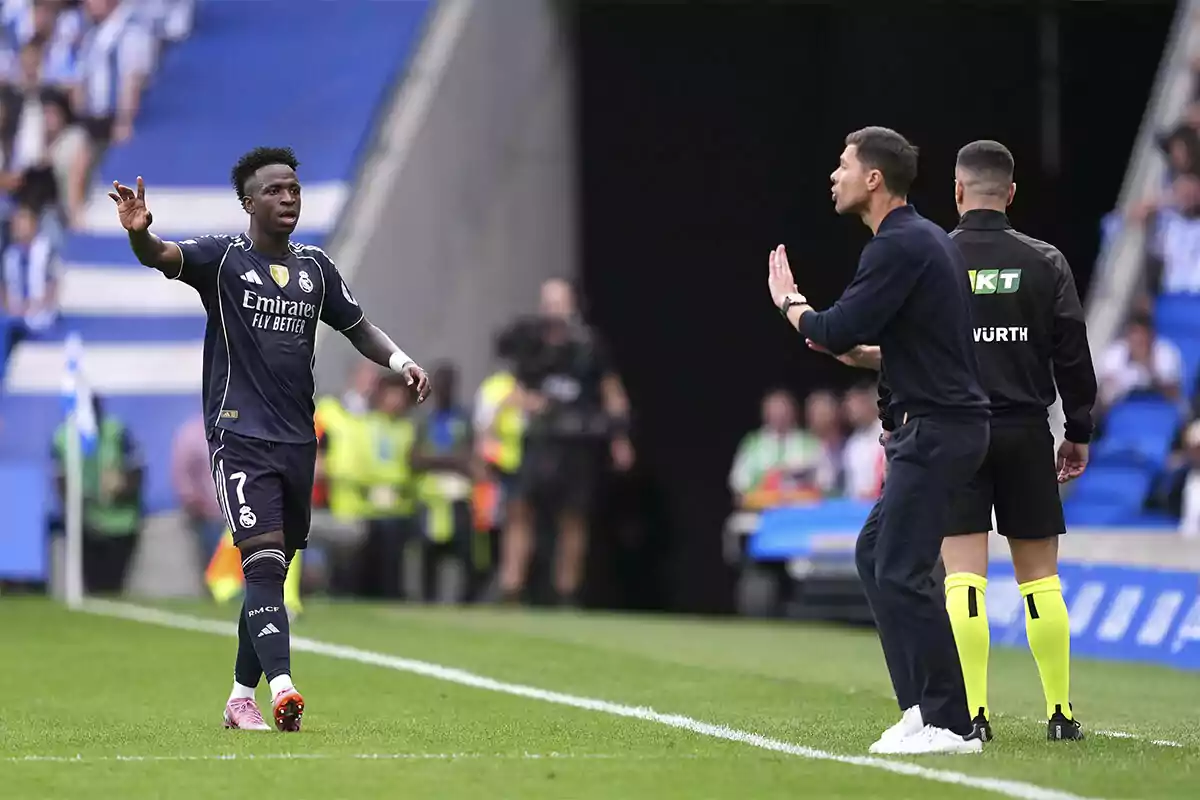 Soccer player in a dark blue uniform gesturing on the field while a coach and a referee watch from the sideline during a match Soccer player in a dark blue uniform gesturing on the field while a coach and a referee watch from the sideline during a match