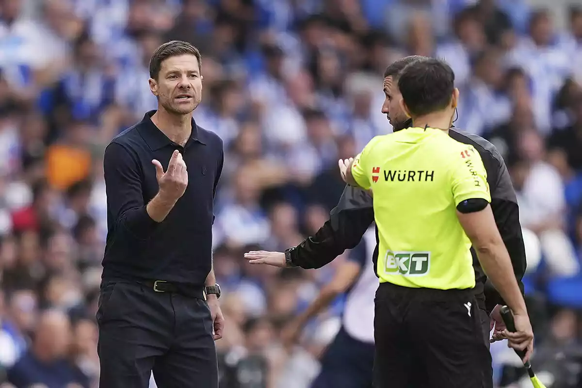 Entrenador de fútbol discutiendo con un árbitro asistente durante un partido, con el público desenfocado al fondo