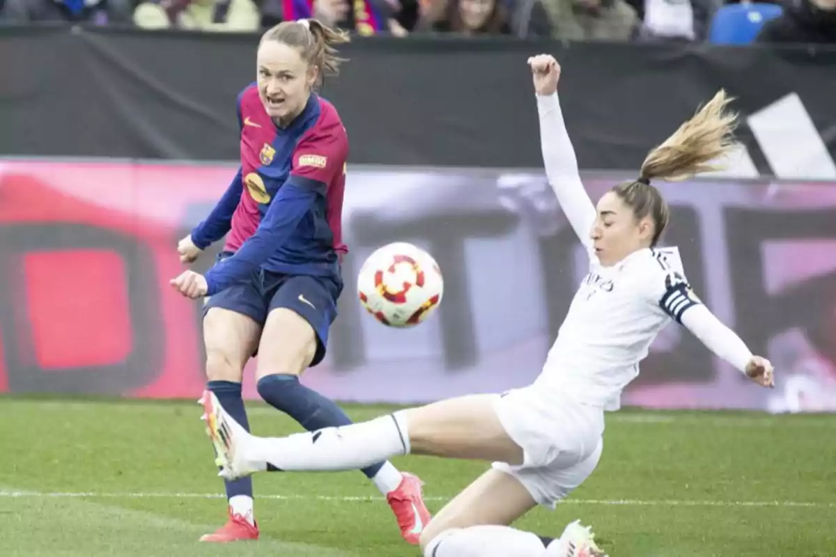 Barcelona female player kicking the ball while a player from the opposing team tries to block in a match. Barcelona female player kicking the ball while a player from the opposing team tries to block in a match.
