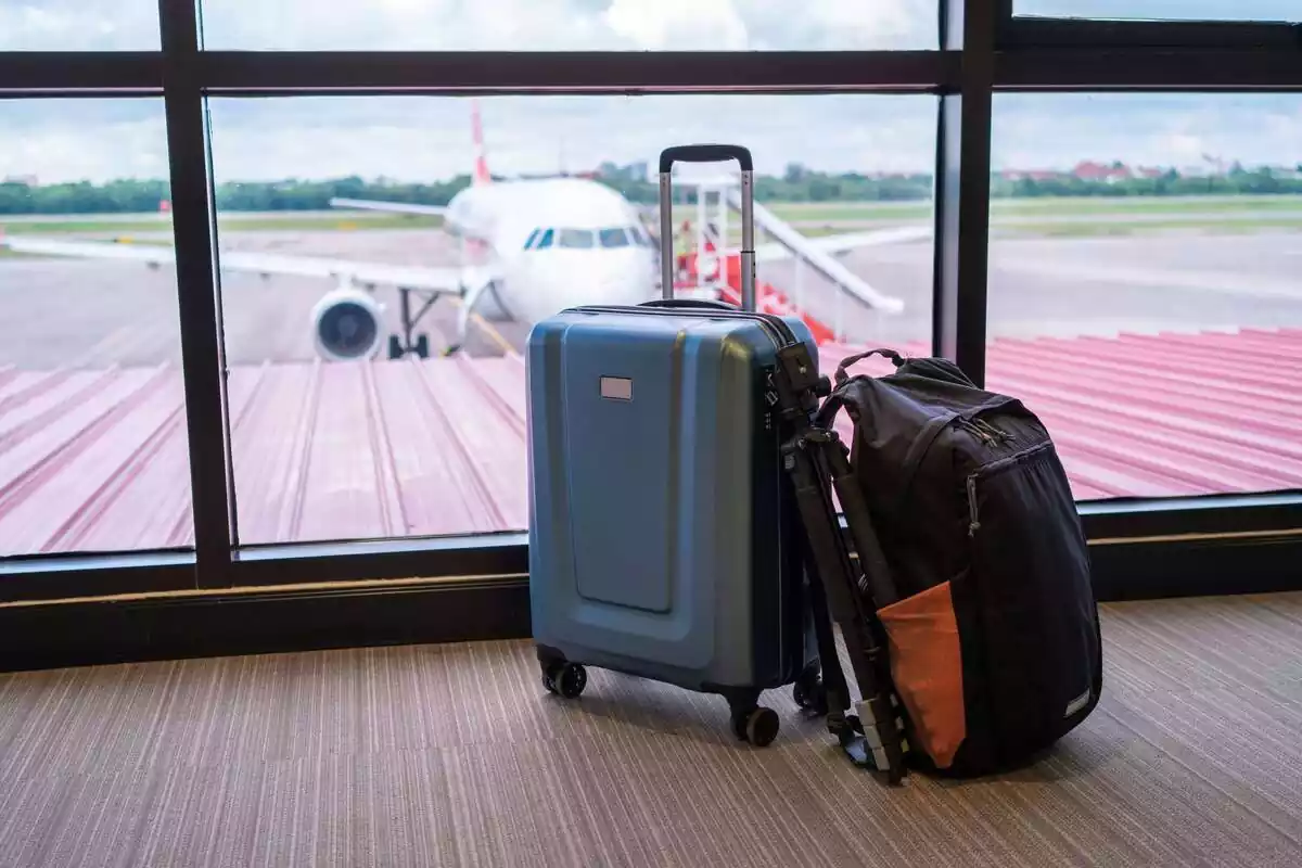 Maletas delante de la ventana de un aeropuerto donde se ve un avión aparcado Maletas delante de la ventana de un aeropuerto donde se ve un avión aparcado
