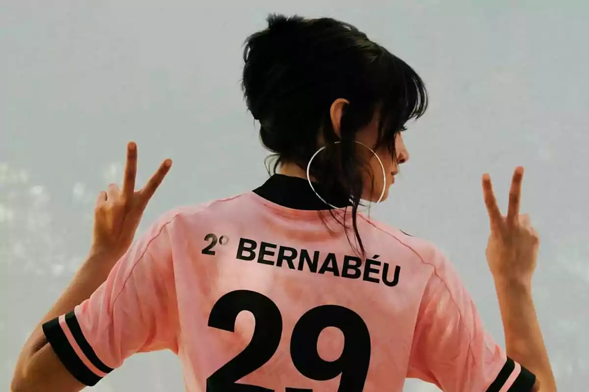 Aitana Ocaña with his back turned wearing a pink jersey with the number 29 and the name Bernabéu, making the peace sign with both hands. Aitana Ocaña with his back turned wearing a pink jersey with the number 29 and the name Bernabéu, making the peace sign with both hands.