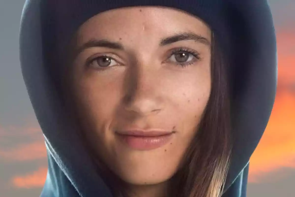 Close-up of a person with a blue hoodie and a sunset sky background.