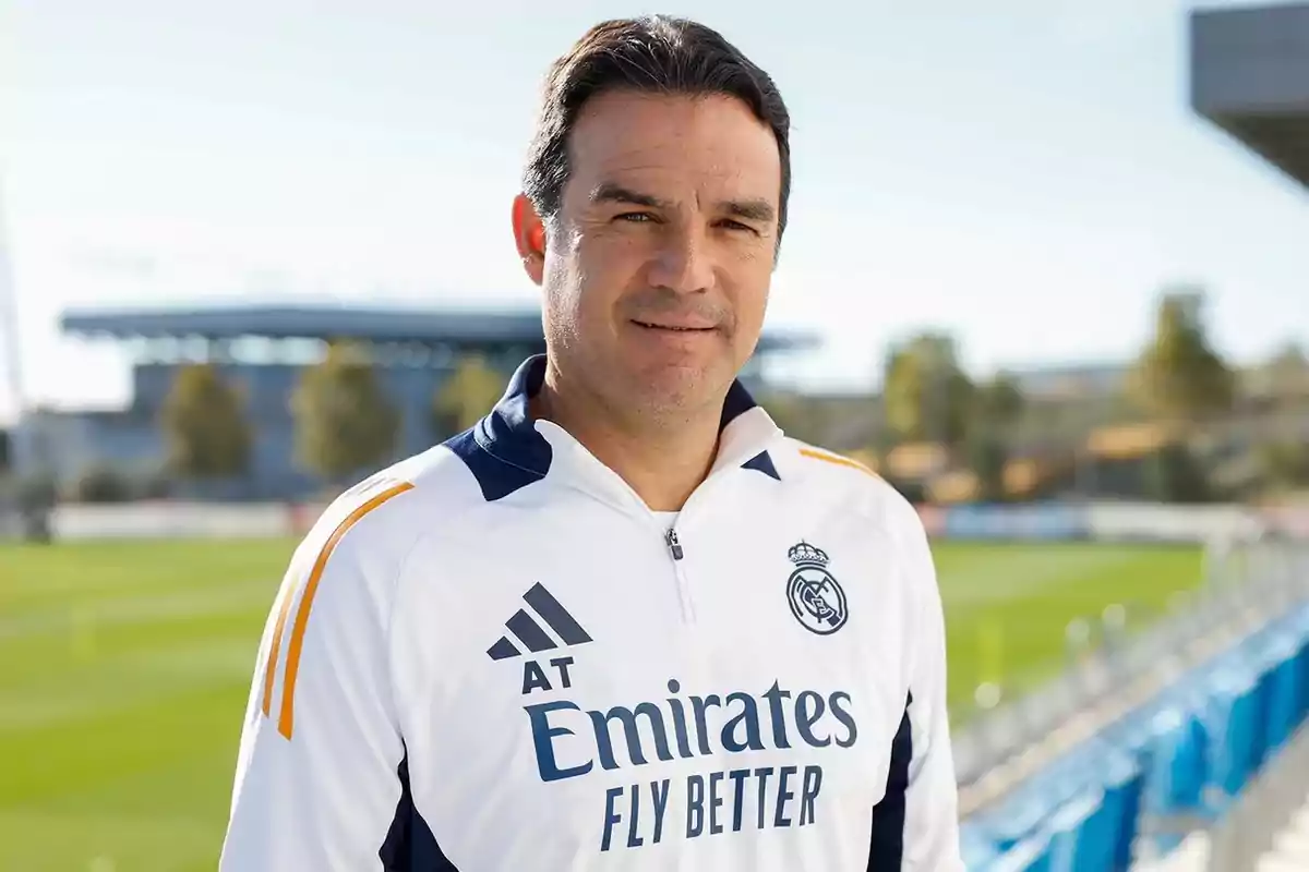 Man wearing a white Real Madrid jacket posing on a soccer field during the day Man wearing a white Real Madrid jacket posing on a soccer field during the day