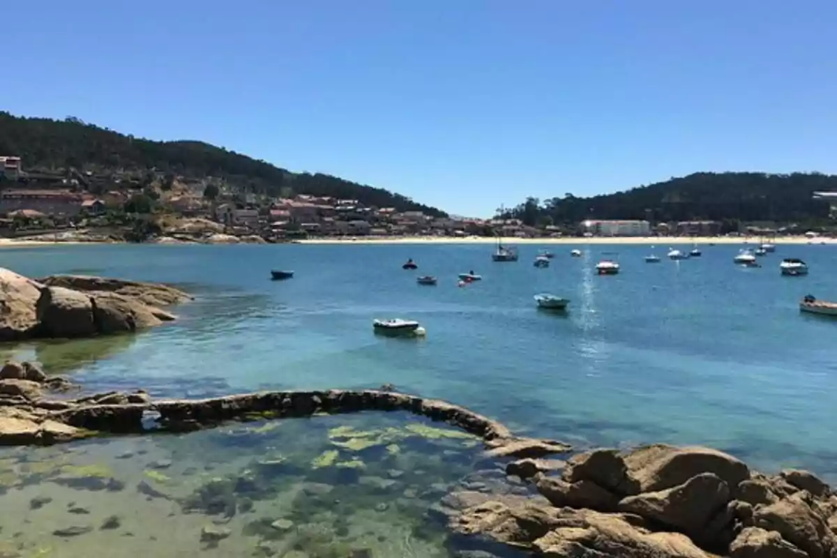 Vista de una bahía con aguas cristalinas, pequeñas embarcaciones flotando y un pueblo costero al fondo. Vista de una bahía con aguas cristalinas, pequeñas embarcaciones flotando y un pueblo costero al fondo.