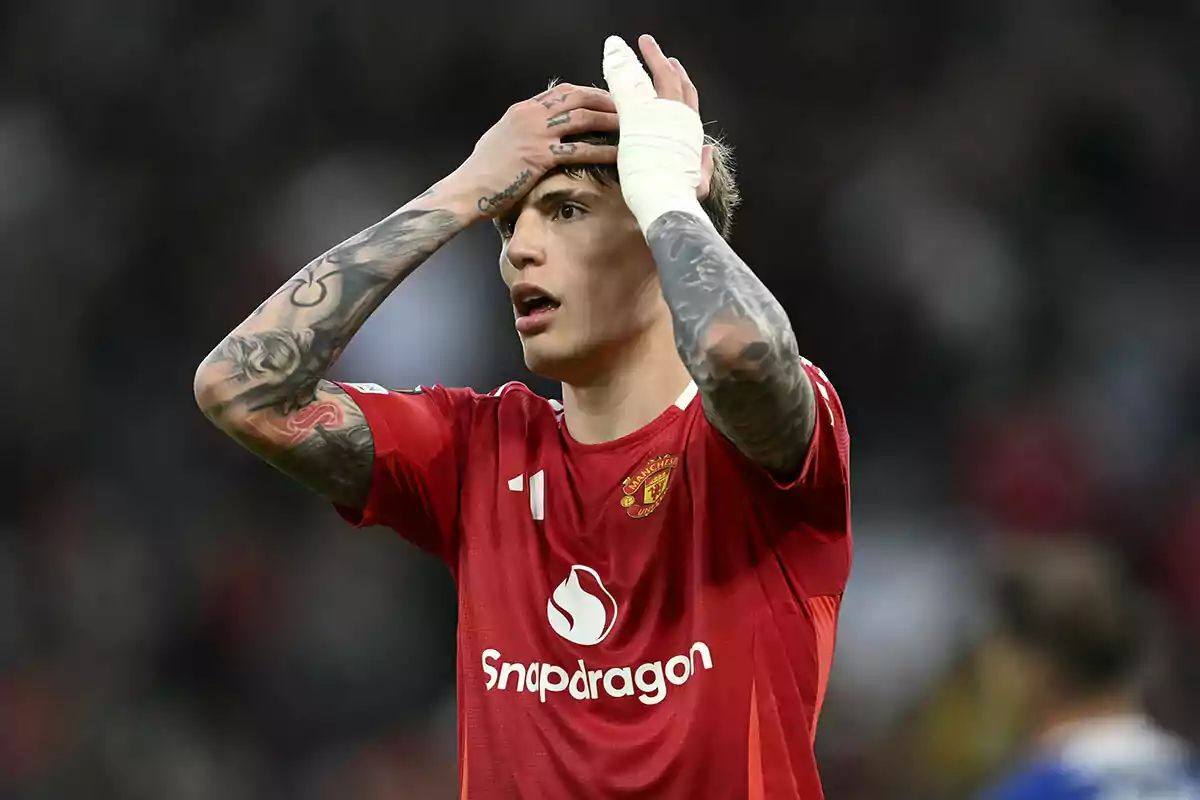 Un jugador de fútbol con uniforme rojo se lleva las manos a la cabeza en un gesto de sorpresa o frustración durante un partido. Un jugador de fútbol con uniforme rojo se lleva las manos a la cabeza en un gesto de sorpresa o frustración durante un partido.