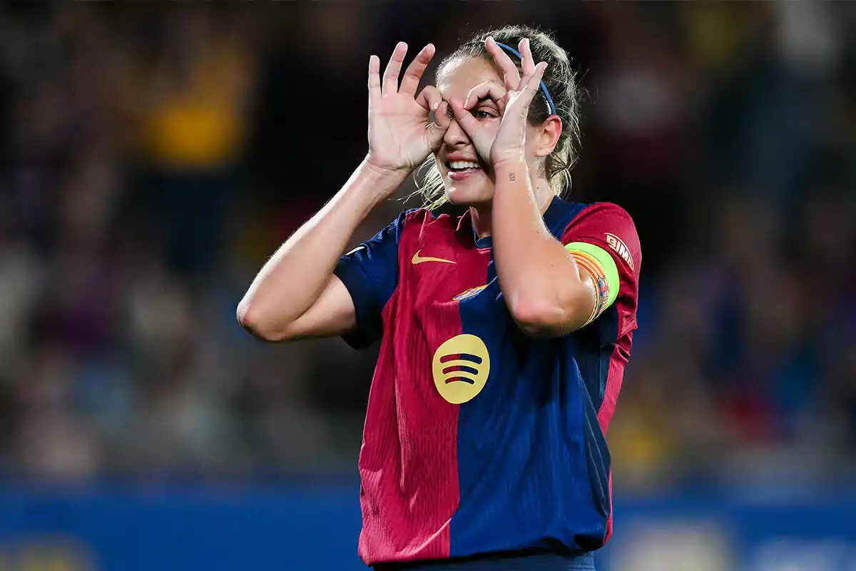 Alexia Putellas in a blue and red uniform makes a funny hand gesture on the field.