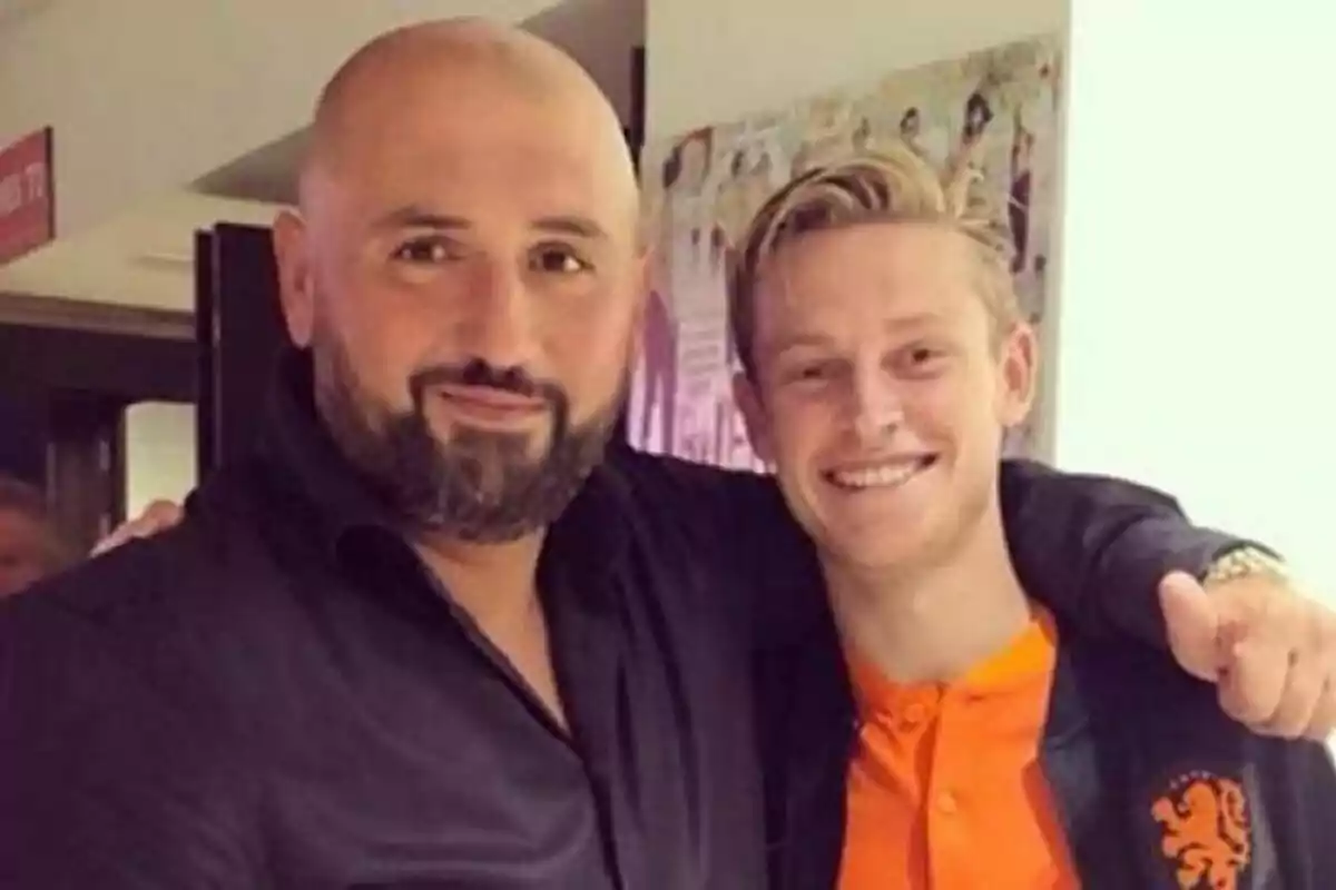 Dos hombres posan juntos y sonríen a la cámara, uno de ellos lleva una chaqueta negra y el otro una camiseta naranja Dos hombres posan juntos y sonríen a la cámara, uno de ellos lleva una chaqueta negra y el otro una camiseta naranja