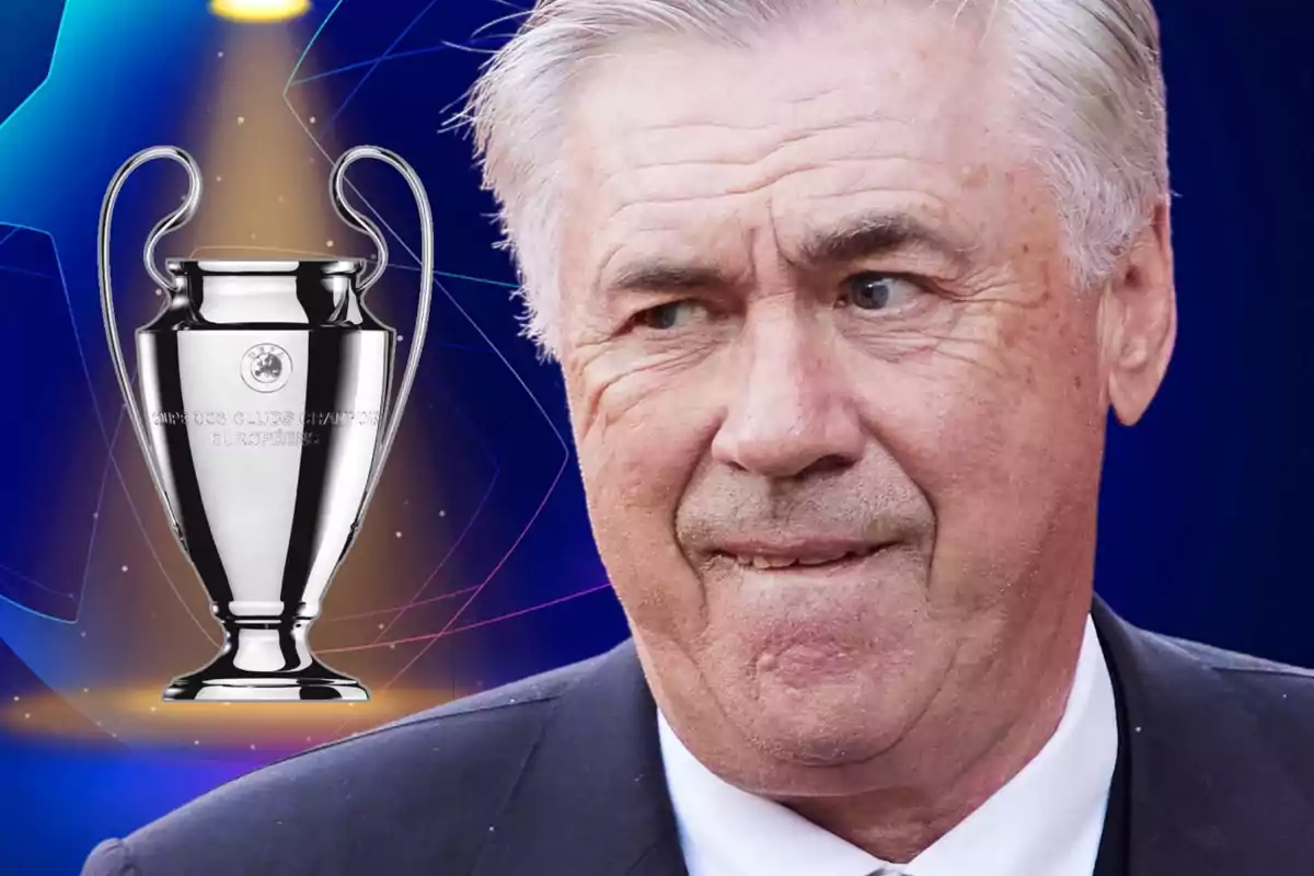 A grey-haired man with a serious expression stands next to a Champions League trophy against a blue background.