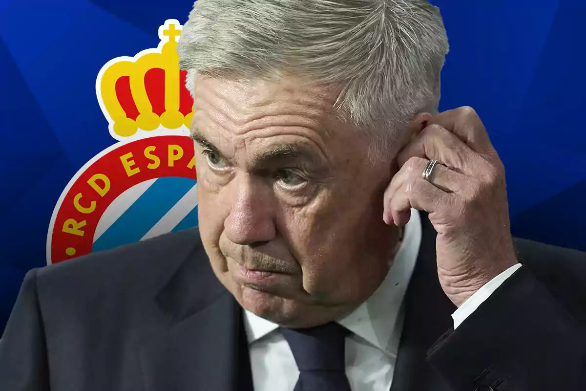 Carlo Ancelotti con traje oscuro se toca la oreja frente a un fondo con el escudo del RCD Espanyol.