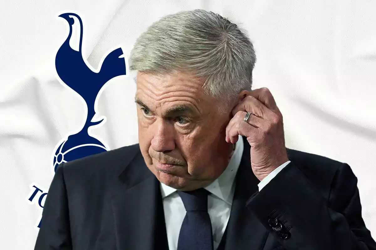 Carlo Ancelotti en traje oscuro se toca la oreja frente al logo del Tottenham Hotspur.