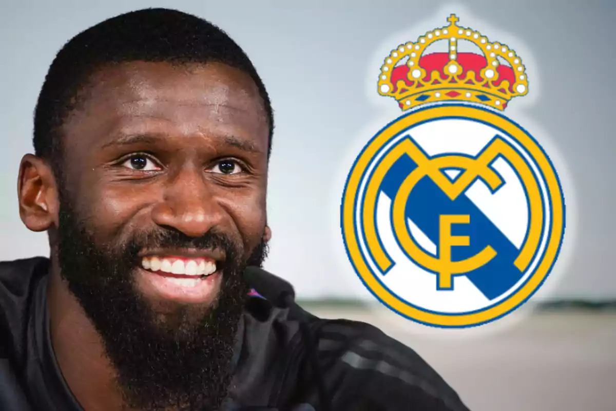 Un hombre sonriente con barba junto al escudo del Real Madrid.