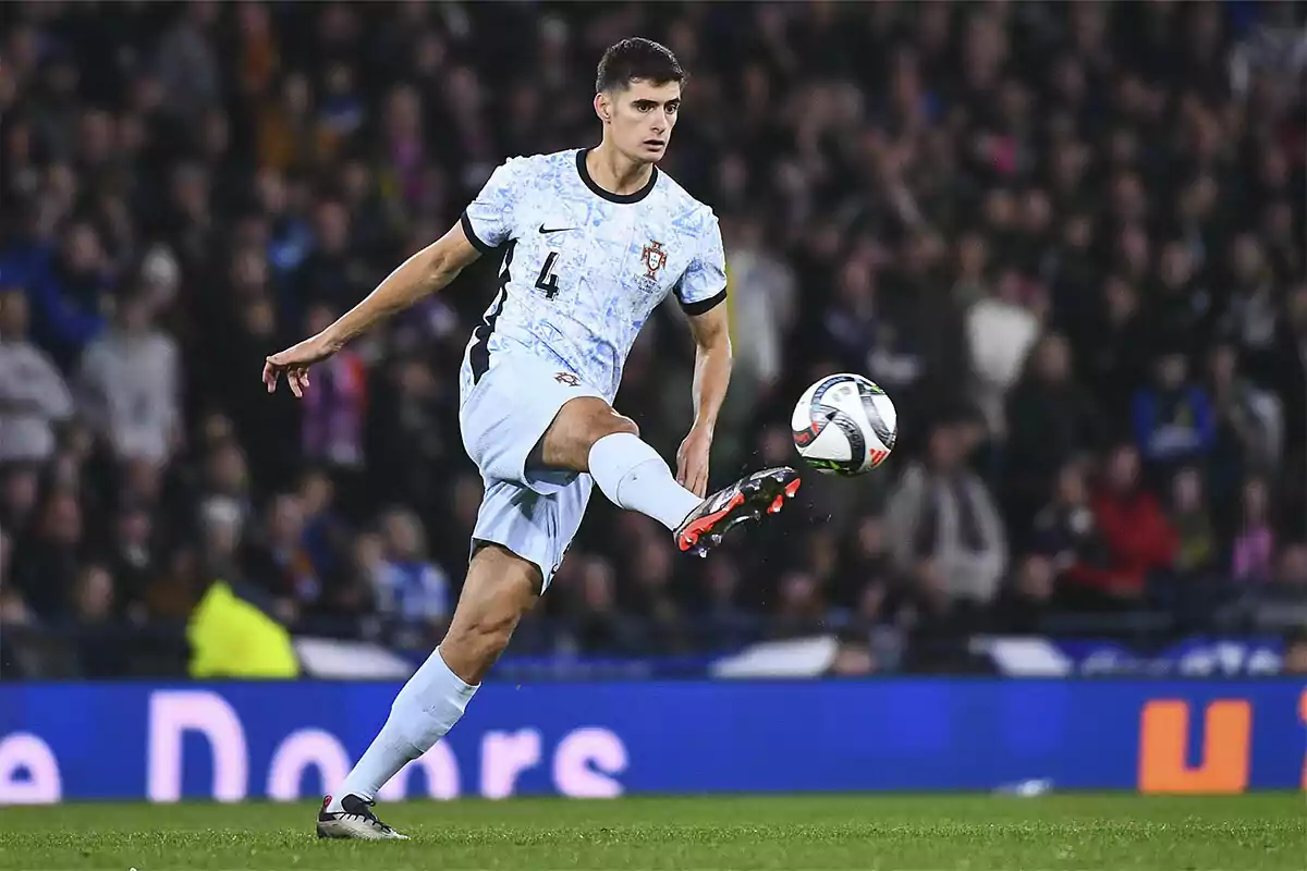 António Silva in a light uniform controls the ball in the air during a match with a crowd of spectators in the background.