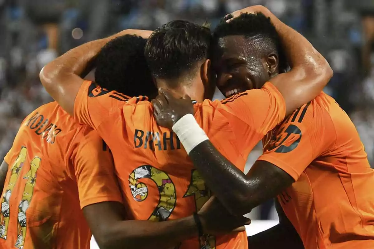 Rodrygo, Brahim y Vinicius celebrando un gol con abrazos en el campo.