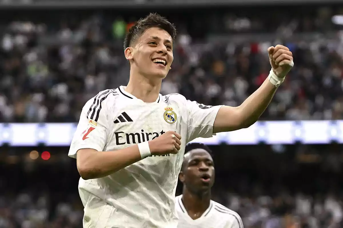 Un jugador de fútbol del Real Madrid celebra en el campo con una expresión de alegría mientras otro jugador aparece al fondo. Un jugador de fútbol del Real Madrid celebra en el campo con una expresión de alegría mientras otro jugador aparece al fondo.