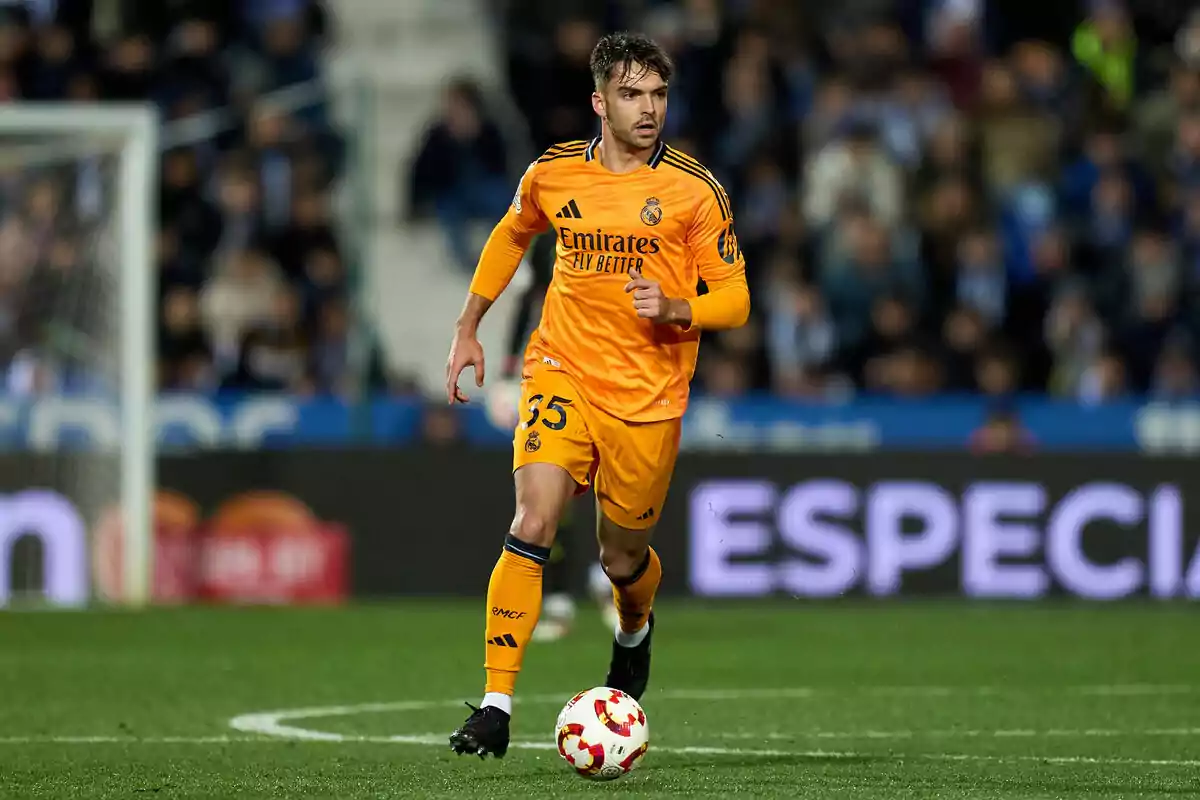 A player in an orange Real Madrid uniform runs on the field during a match.