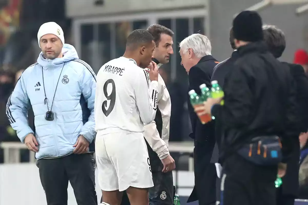 A group of people wearing sportswear and warm clothing chat in an environment that appears to be a soccer stadium. A group of people wearing sportswear and warm clothing chat in an environment that appears to be a soccer stadium.