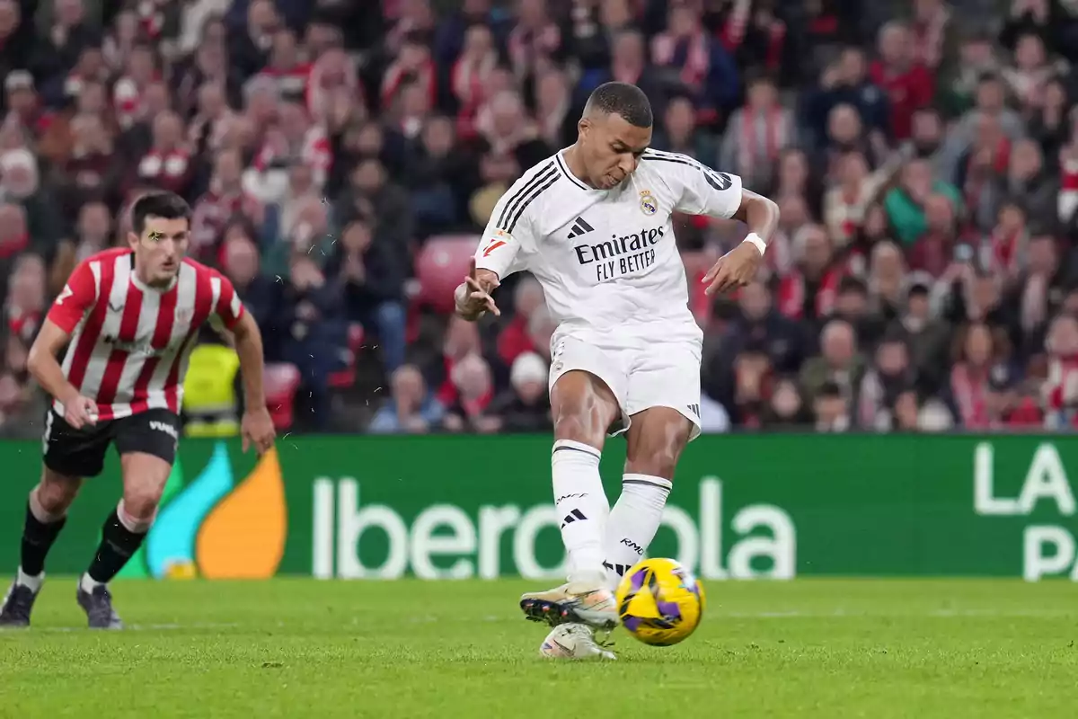 A Real Madrid soccer player kicks the ball during a match while a player from the opposing team watches.