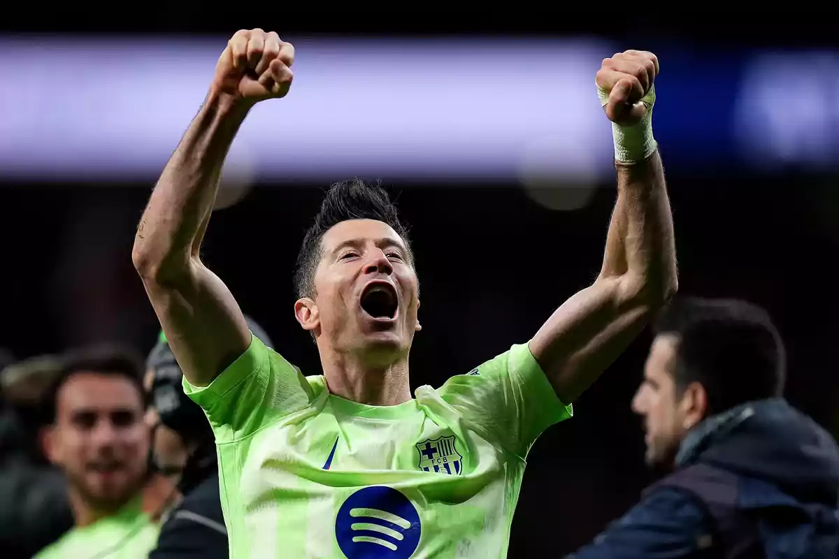 A player celebrates with arms raised wearing a green jersey in a stadium.