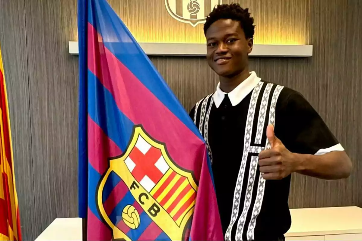 A smiling young man holds an FC Barcelona flag while giving a thumbs-up. A smiling young man holds an FC Barcelona flag while giving a thumbs-up.