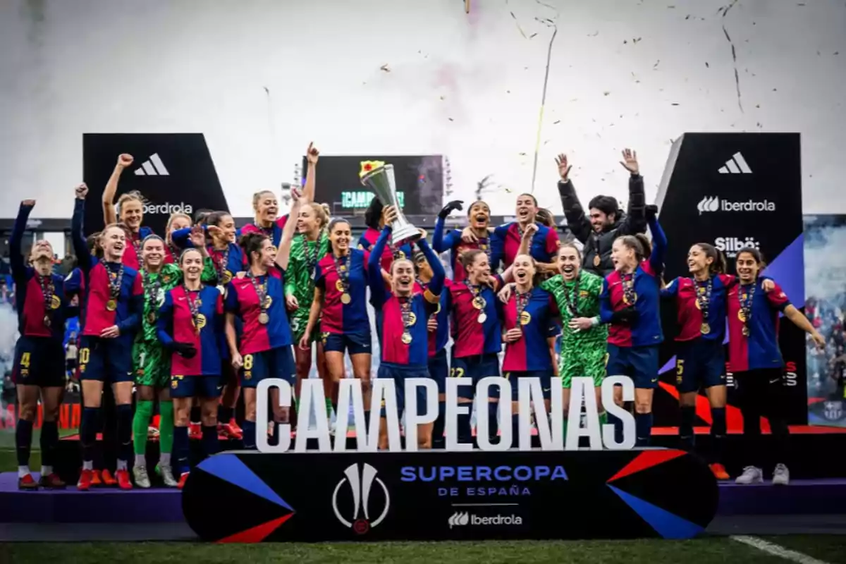 A women's soccer team celebrates with a trophy and medals on the podium of the Spanish Super Cup, with confetti falling around them.