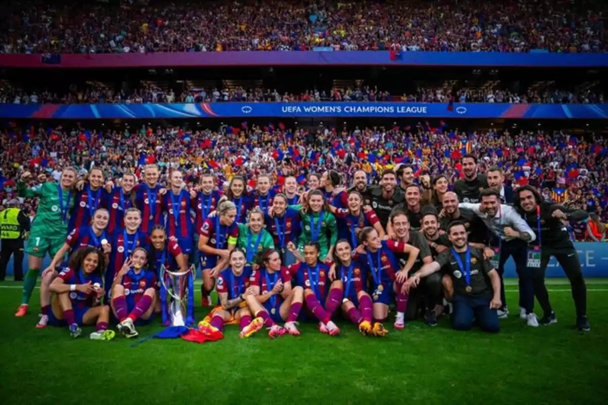 A women's soccer team celebrates on the field with a trophy, surrounded by a crowd of fans in the stadium.