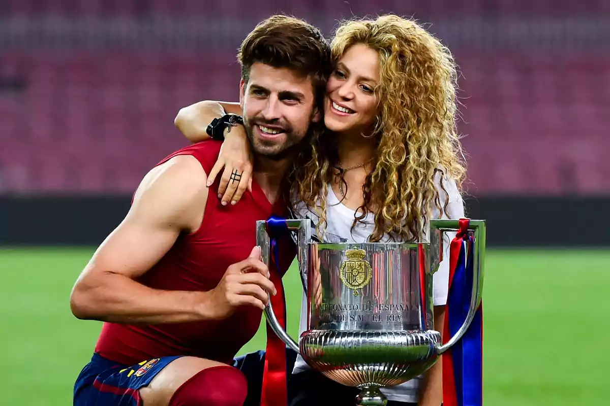 A smiling couple poses with a trophy at a soccer stadium.