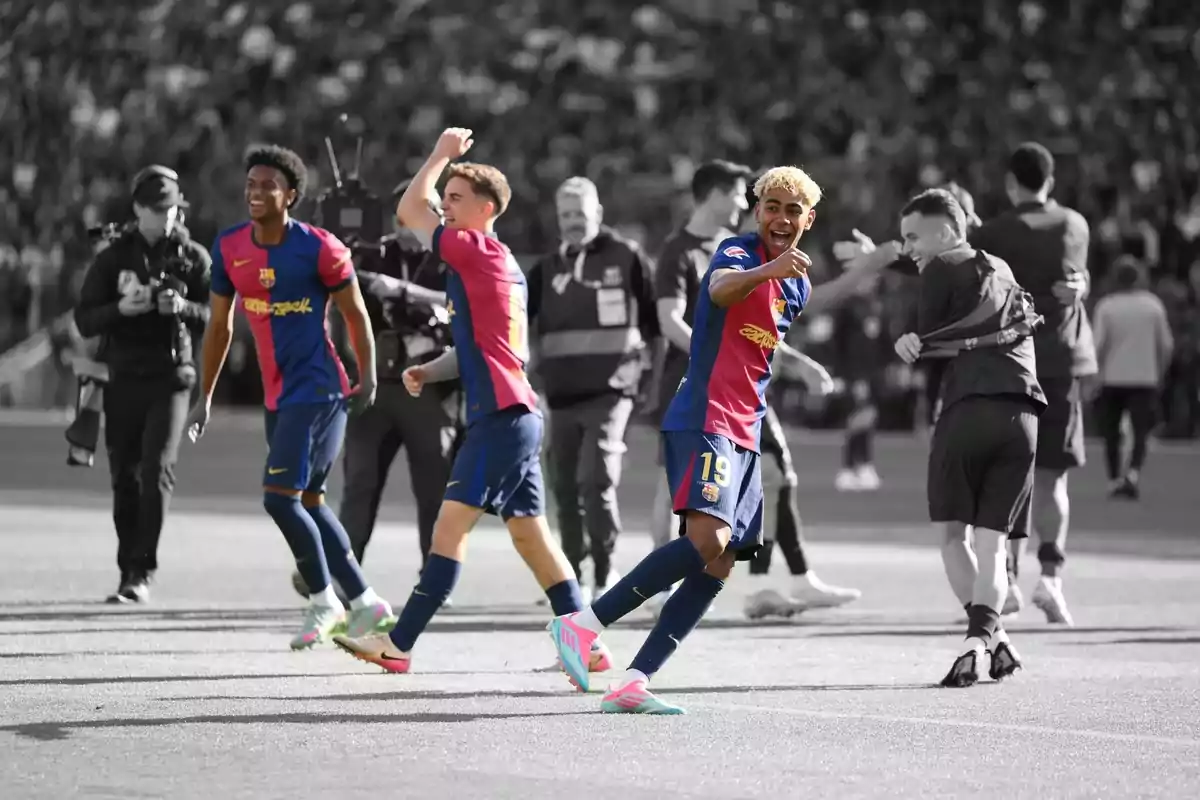 Jugadores de fútbol celebrando en el campo con uniformes azul y rojo, mientras el fondo está en blanco y negro.