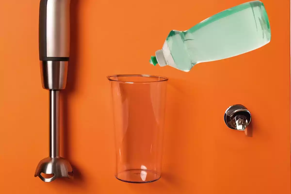 Una licuadora de mano, un vaso de plástico, una botella de detergente y una llave de agua sobre un fondo naranja.