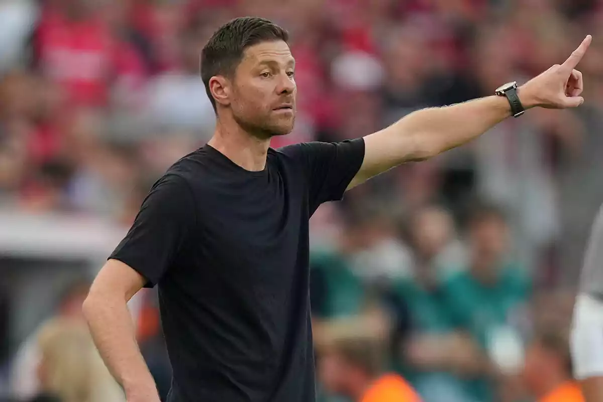 Xabi Alonso con camiseta negra señalando con el dedo índice en un entorno deportivo.