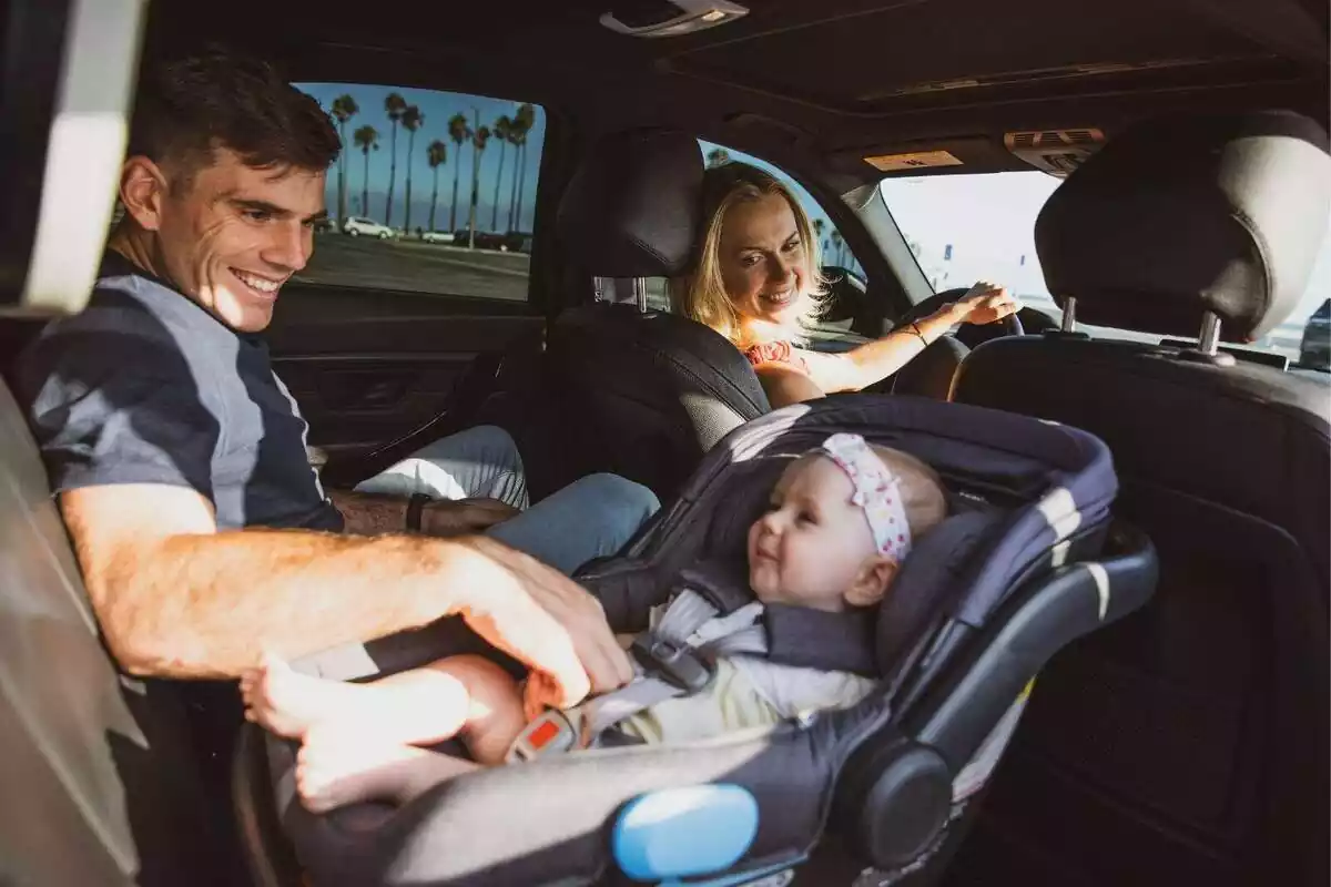 Plano general de una familia dentro de un coche, la madre conduciendo y el padre detrás con el bebé en la sillita del coche