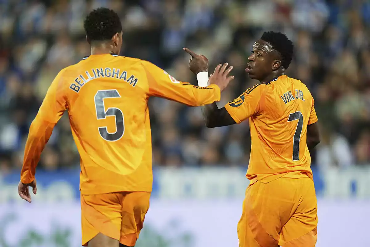 Two soccer players in orange uniforms interact on the field during a match.