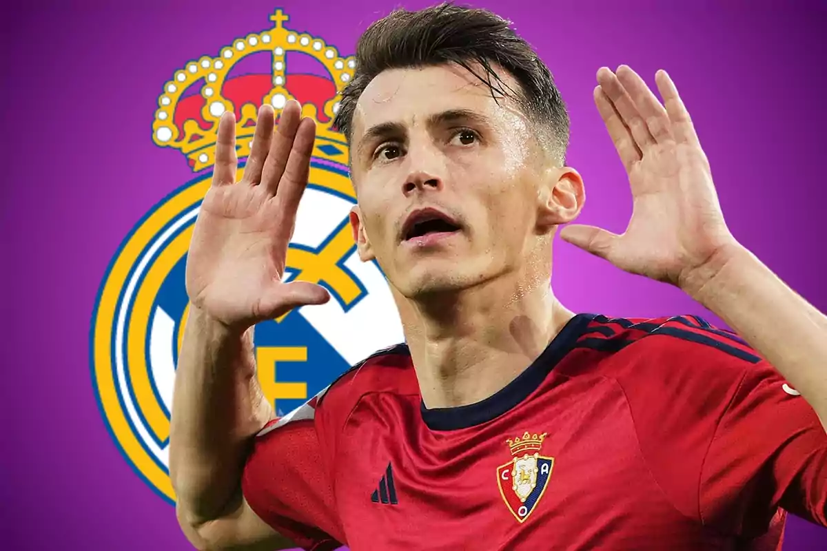 Futbolista con uniforme rojo celebrando con las manos cerca de las orejas frente al escudo del Real Madrid sobre un fondo morado