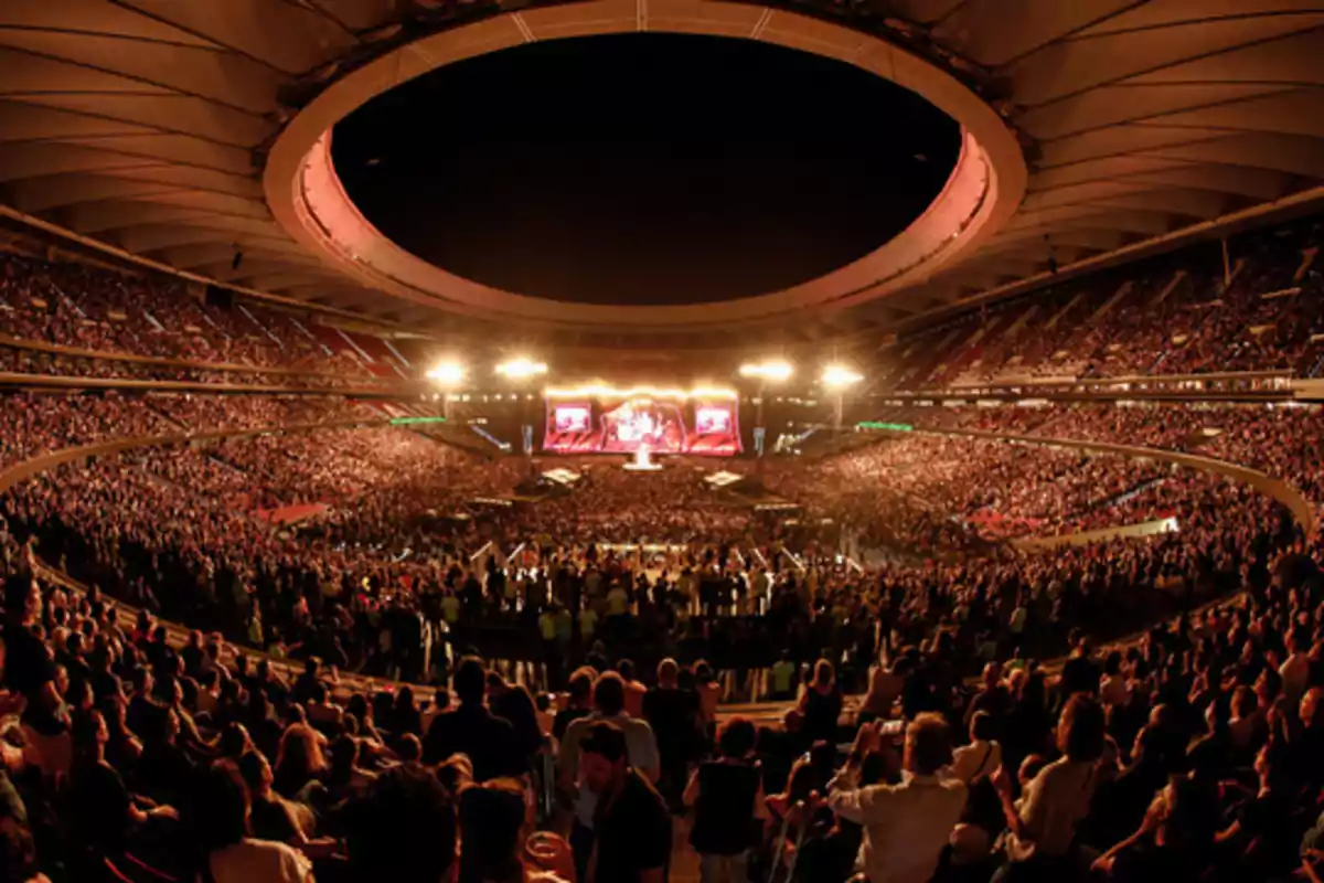 A stadium full of people enjoying a nighttime concert with bright lights illuminating the stage.