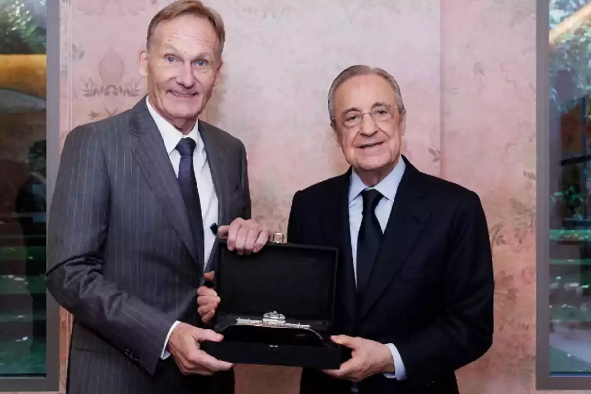 Two men in suits pose together holding a black case with a silver object inside.