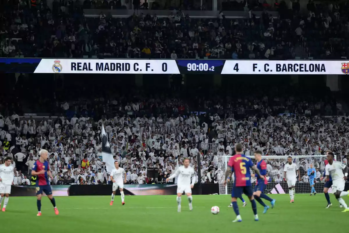 A soccer match between Real Madrid and FC Barcelona with the score showing 0-4 in favor of Barcelona and a crowd of fans in the stands.