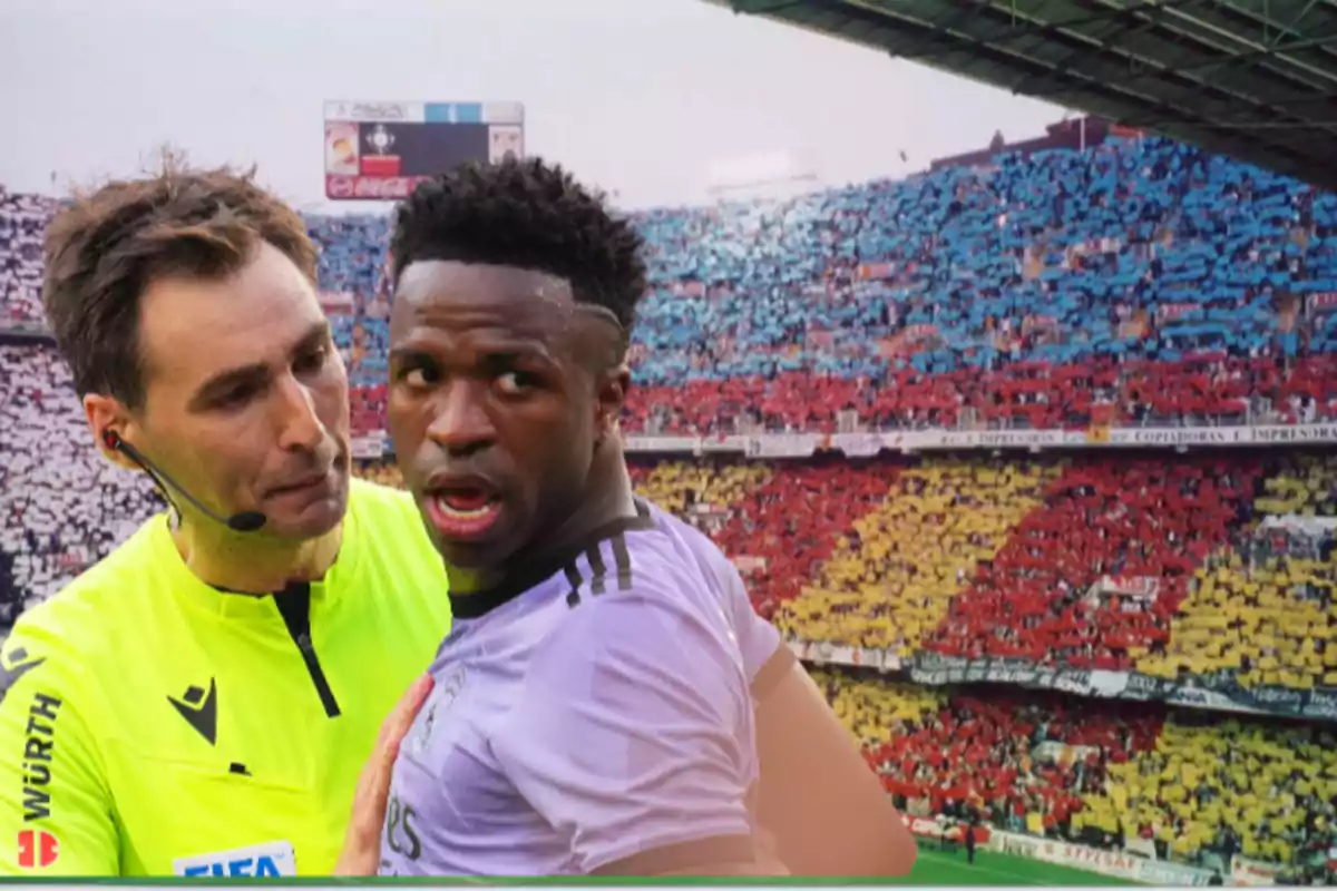 A soccer referee talks to a player on the field, with a stadium full of fans in the background.