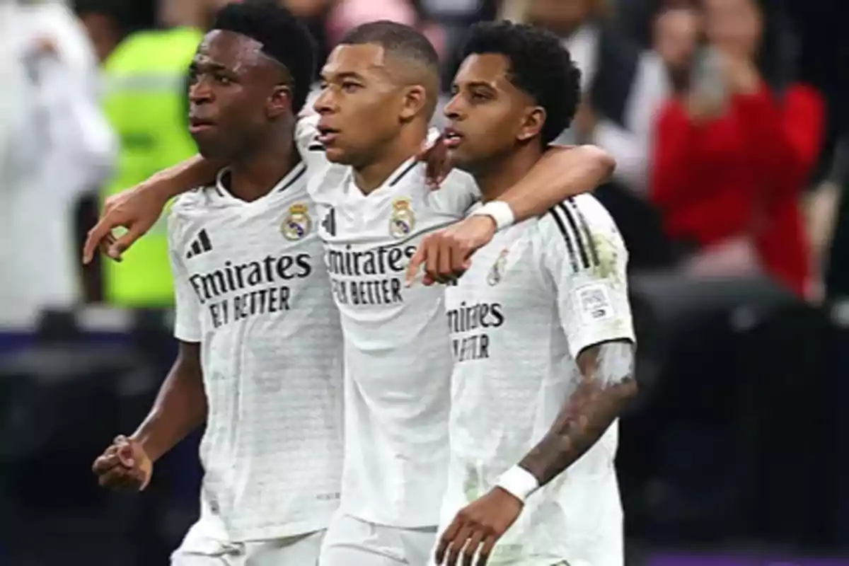 Three soccer players in white uniforms celebrate together on the field.