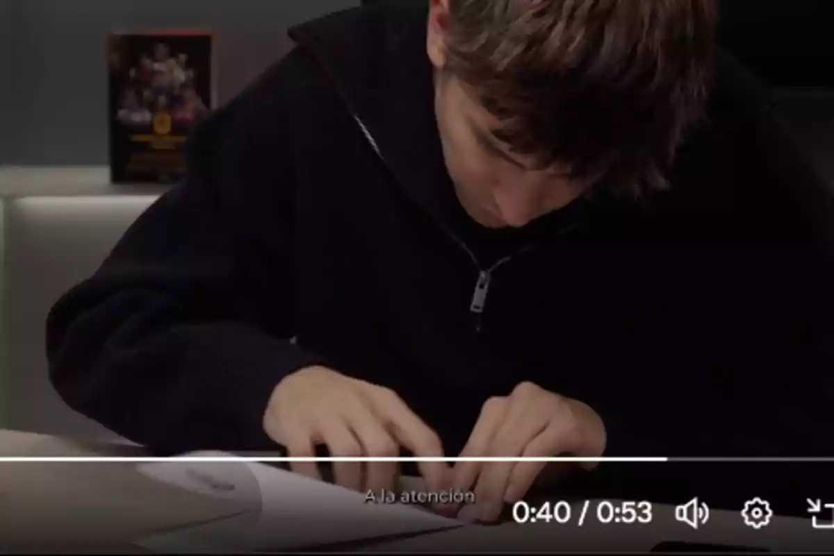 A young man in a black sweater is concentrating on writing on a piece of paper on a table.